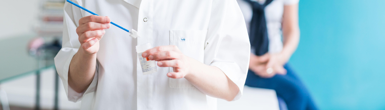 Image of doctors hands preparing a cervical screening test with female patient in the background.