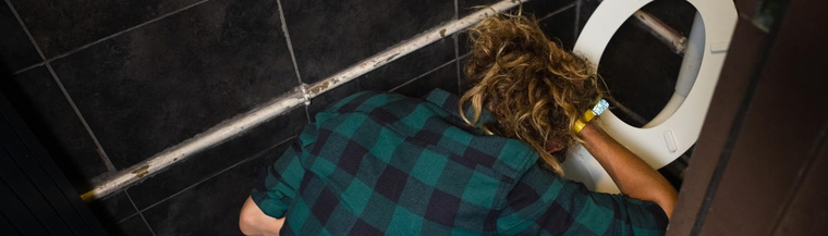 Man vomiting on toilet bowl in the washroom to illustrate binge drinking Man vomiting on toilet bowl in the washroom to illustrate binge drinking